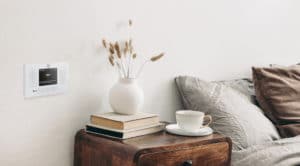 Modern white ceramic vase with dry Lagurus ovatus grass and cup of coffee on retro wooden bedside table. Beige linen and velvet pillows in bedroom, scandinavian interior. Homestaging.