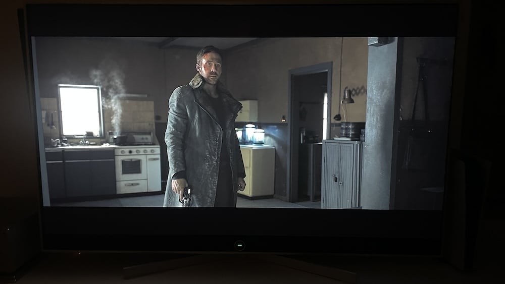 a man in a leather coat holding a gun in a kitchen